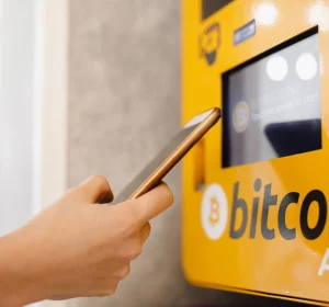 Close-up of a person using a smartphone near a Bitcoin ATM terminal