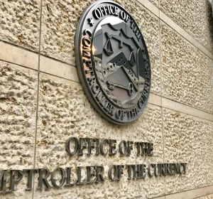 Office of the Comptroller of the Currency seal and signage on a building exterior, suitable for banking regulation coverage.