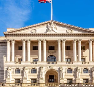 Union Jack flying above a grand neoclassical building with columns under a bright blue sky.