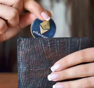 Hand placing a silver Ethereum token into a dark textured wallet