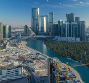 Aerial view of Abu Dhabi's coastal skyline with modern skyscrapers, a waterway, mangroves, and an active construction site