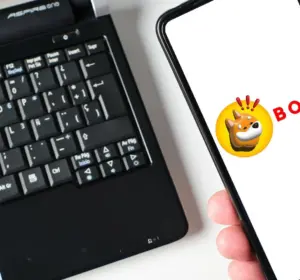 Person holding a smartphone displaying the BONK cryptocurrency logo next to an Acer Aspire One laptop keyboard