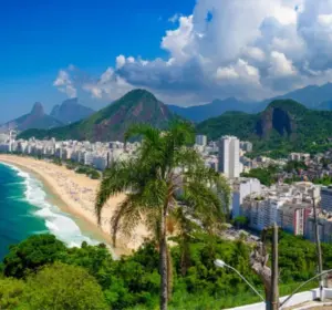 Aerial view of Copacabana Beach in Rio de Janeiro with a Brazilian flag, palm trees, and mountains in the background