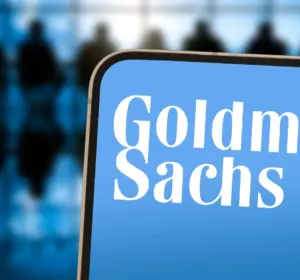 Smartphone displaying the Goldman Sachs logo on a blue screen with silhouetted figures in the blurred background
