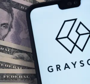 Grayscale logo displayed on a smartphone placed over U.S. dollar banknotes.