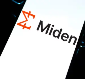 Smartphone screen displaying the Miden logo with an orange geometric icon, resting beside a backlit keyboard
