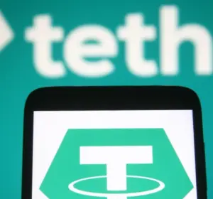 Tether logo displayed on a smartphone with enlarged Tether branding in the background
