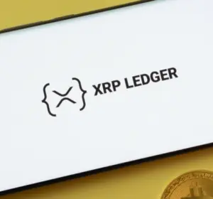 XRP Ledger logo displayed on a smartphone beside gold Bitcoin coins on a yellow background