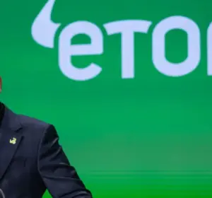 Man in a navy blazer speaking at a podium in front of a large green eToro logo backdrop