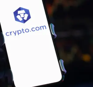 Smartphone displaying the Crypto.com logo with cryptocurrency trading charts blurred in the background.