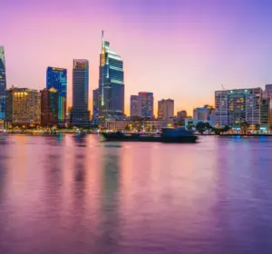 Ho Chi Minh City skyline illuminated at dusk along the Saigon River with modern high-rise buildings.