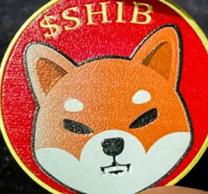 Hand holding a Shiba Inu token featuring the SHIB dog logo against a dark background.